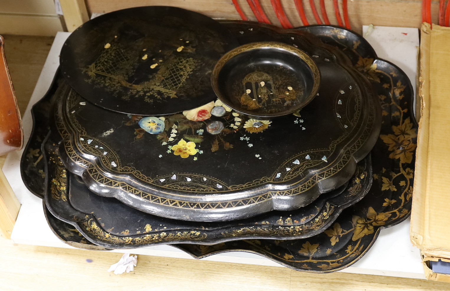 Four papier-mâché-mâché trays, a roundel and bowl, largest tray 80cms wide